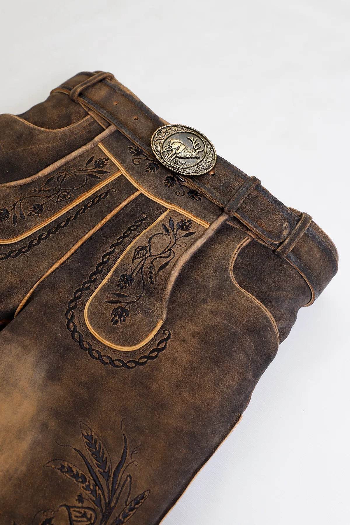 Close-up of dark brown leather lederhosen with stitched decorative panels and metal belt buckle
