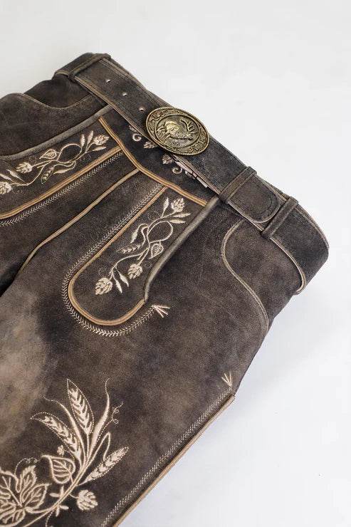Dark suede lederhosen close-up with floral embroidery, ornate stitching, brass belt buckle.