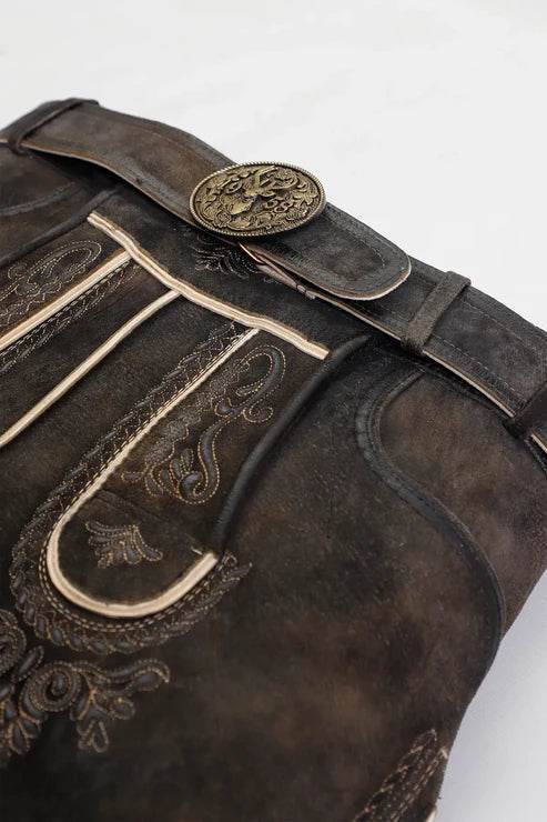 Close-up of dark brown lederhosen with gold embroidery trim and round metal belt buckle.